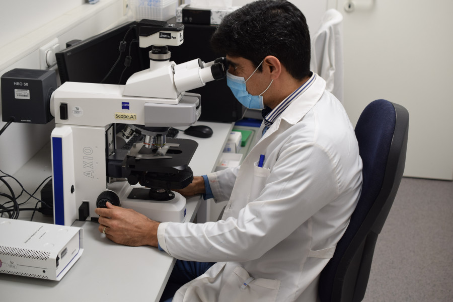 ein Mann im weißen Laborkittel sitzt vor einem Mikroskop und schaut hinein